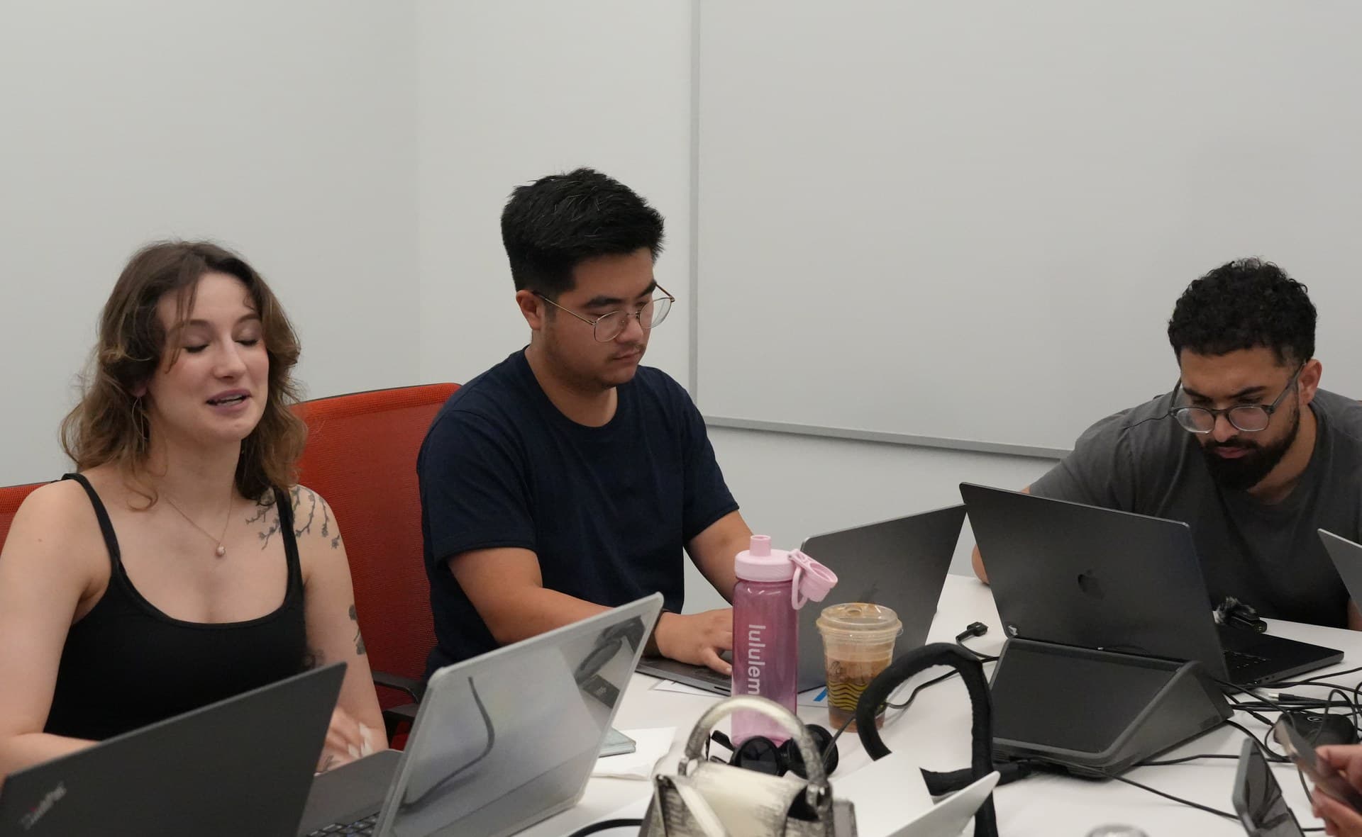 Three attendees working at laptops around a table with a blank whiteboard behind them during a Zero to Agent working session